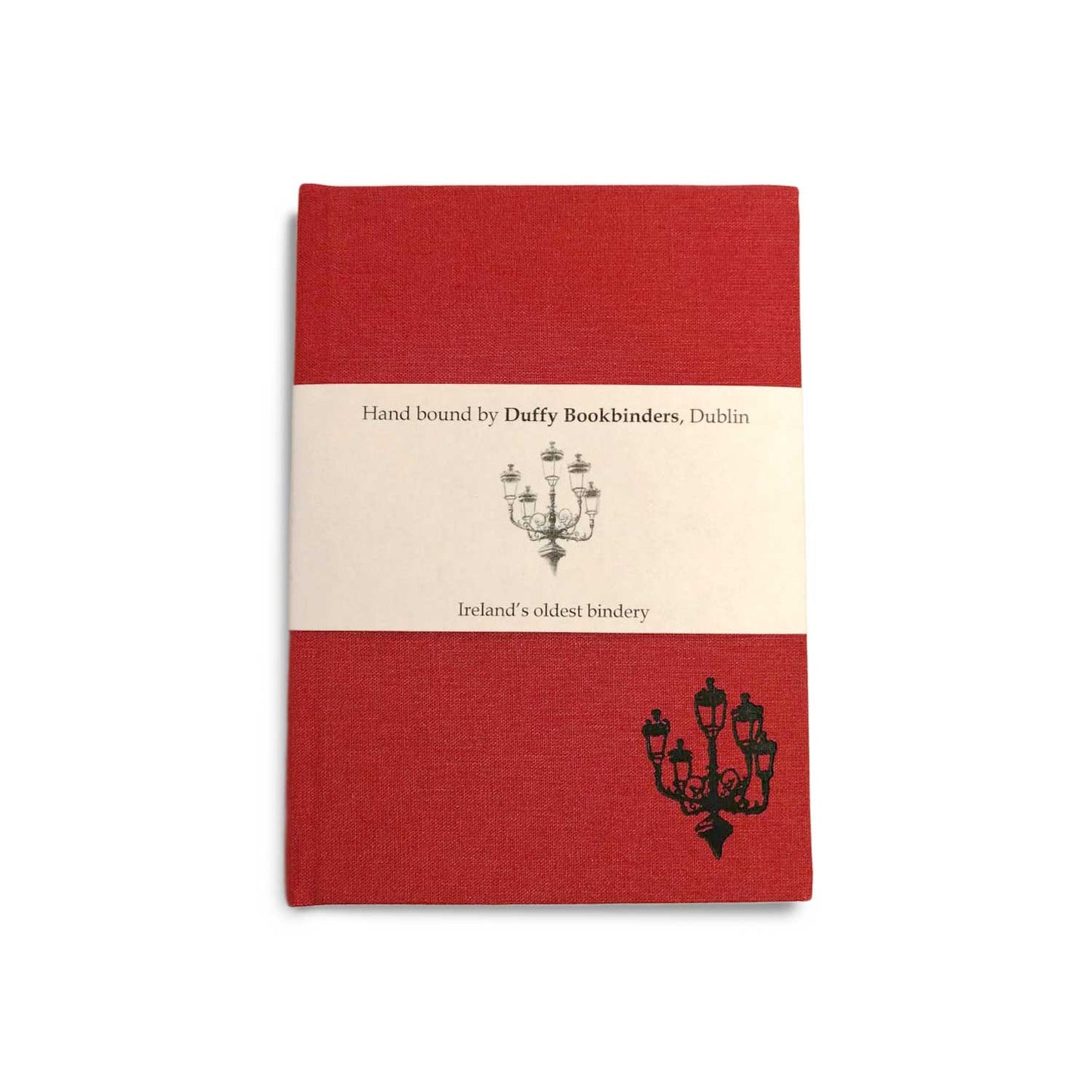 A red clothbound notebook with a cream belly band around the centre. There is a simple line illustration of a street lamp with five lanterns in the bottom right corner of the notebook and on the band.