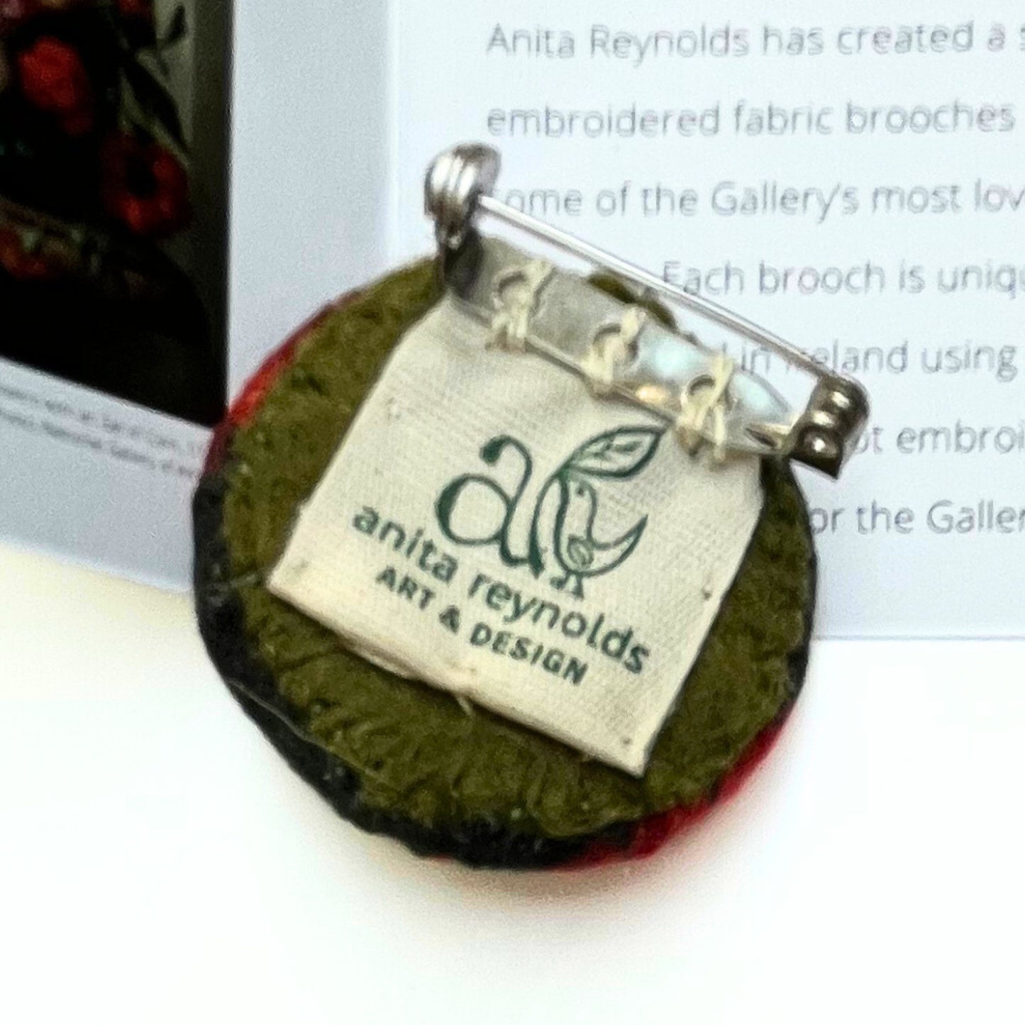 Reverse of fabric brooch with 'anita reynolds art & design' label next to its painting reproduction and box